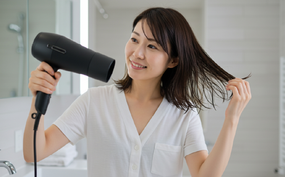 アホ毛を押させながらドライヤーで髪を乾かす女性